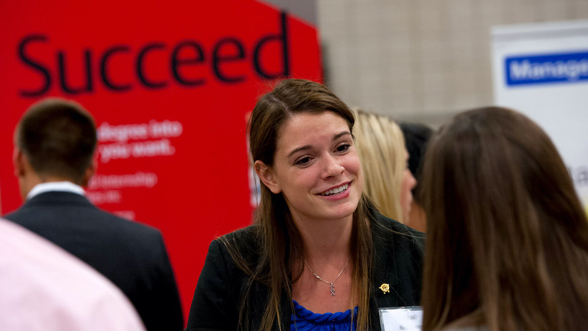 Student greets employer at career fair. The word "success" is in background