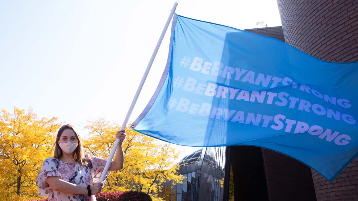Masked Bryant student holding a flying #BeBryantStrong flag