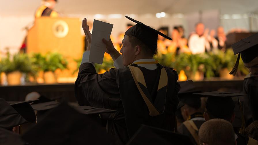Image of student in cap and gown applauding at commencement 