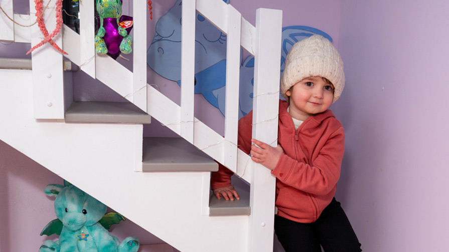 Young girl in pink sweatshirt sitting on playhouse stairs.