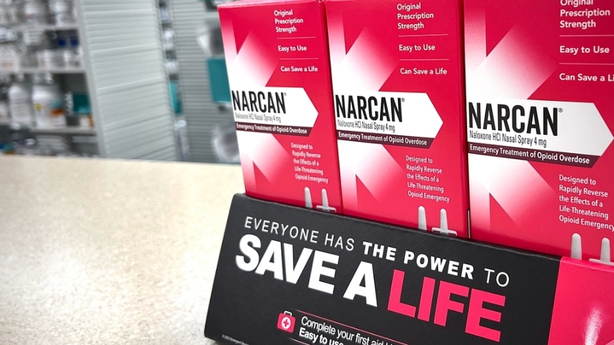 Three Narcan boxes sit on a pharmacy countertop.