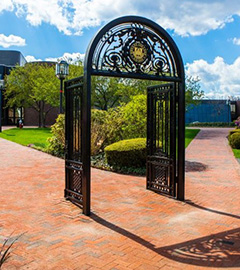     The Bryant University archway against a blue sky casts a beautiful shadow on the brick walkway..
