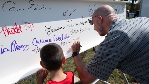 Members of the Bryant community make their mark on university history by signing the final beam to be placed in the construction of the new Bryant University Fieldhouse at the entrance to the David M. '85 and Terry Beirne Stadium Complex.