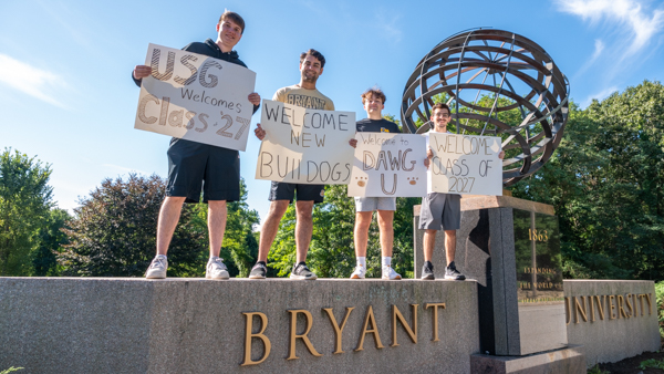 Students with welcome signs at university entrance.