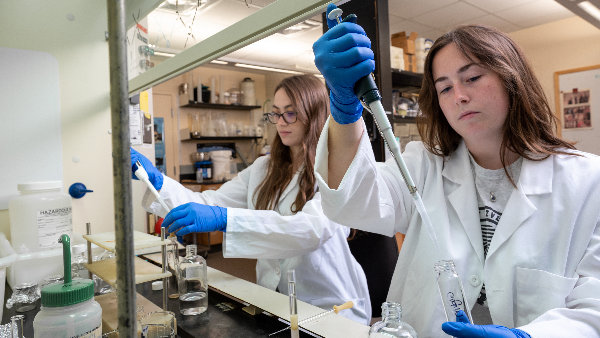 Two science students using pipets under fume hood