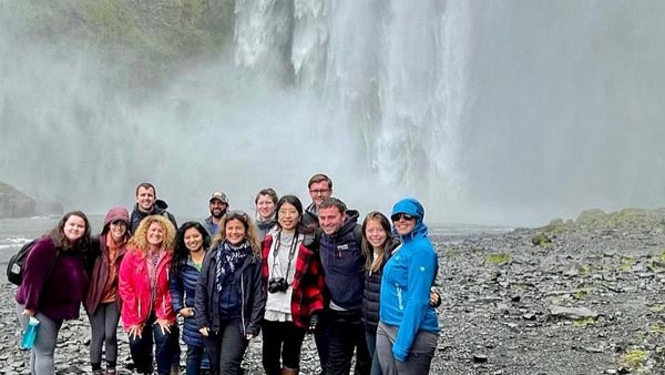 Students post for group photo in front of waterfall